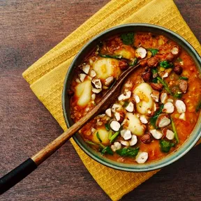 Photo of curry soup with gnocchi and lentils in a bowl with a wooden spoon