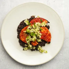 Foto van gekaramelliseerde gochujang knolselderij uit de oven met zwarte bonen en groene salsa