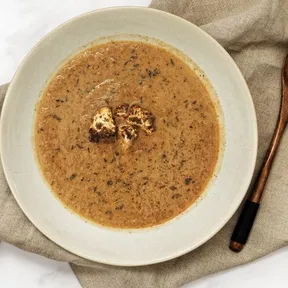 Photo of a bowl of roasted cauliflower soup with a wooden spoon