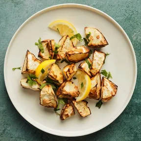 Geroosterde knolselderij uit de airfryer op een bord, gegarneerd met partjes citroen en koriander