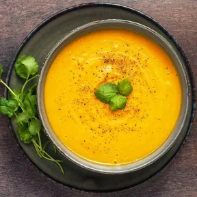 Foto van een kom geroosterde pompoensoep met kokosmelk, gegarneerd met verse koriander en zwarte peper