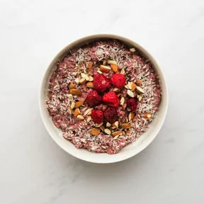 Photo of a white bowl of oatmeal with raspberries, coconut and almonds