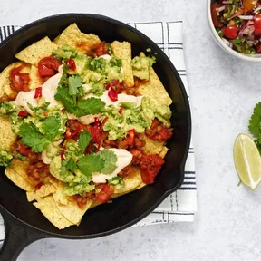 Lentil nacho bowl in a cast iron pan with pico de gallo and lime on the side