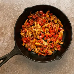 Foto van een gietijzeren skillet met shoarma van oesterzwammen met paprika en rode ui