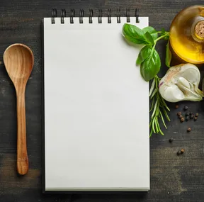 Stock photo of a notebook with ingredients around it. Photo sourced from Adobe Stock.