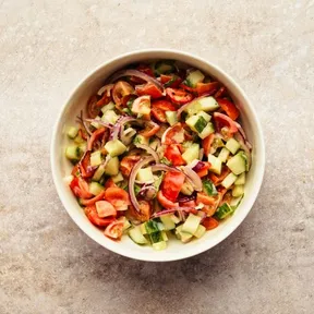 Foto van een kommetje met salade van komkommer en cherrytomaten met een dressing van tahin en citroen