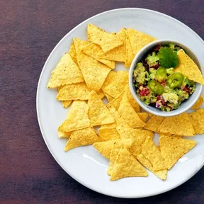 Guacamole in a bowl on a plate with tortilla chips